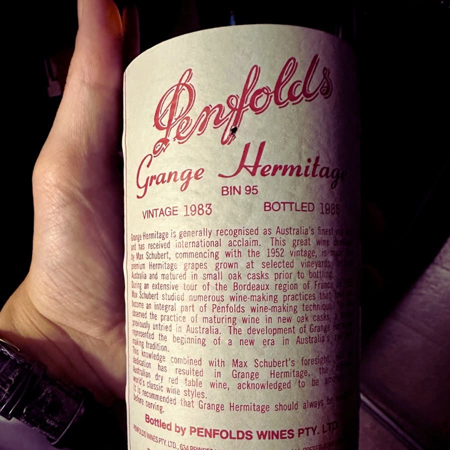 A hand holding a bottle of Penfolds Grange Hermitage Bin 95, Vintage 1983, Bottled 1985, with a cream label in red script