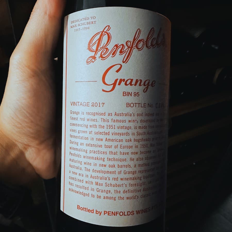 A hand holding a bottle of Penfolds Grange Bin 95, Vintage 2017, with a white label dedicated to Max Schubert, 1915 to 1994