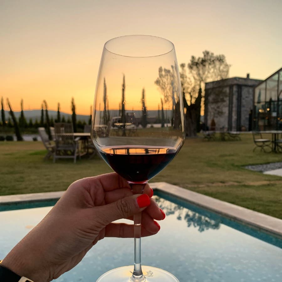 A glass of red wine held up against the sunset at a winery in Urla